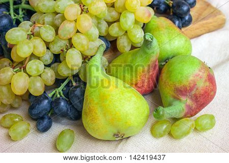 Still life - bright fruit on light fabric. Vintage black and green grapes fragrant pear. Concept - healthy food.