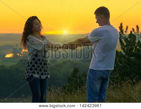 romantic couple holding hands at sunset on outdoor, beautiful landscape and bright yellow sky, love tenderness concept, young adult people