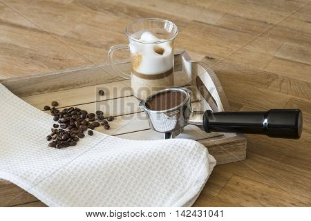 Glass of latte macchiato, coffee beans and a grouphead on a wooden tray