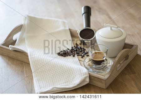 Glass of espresso, brown sugar, coffee beans, grouphead and sugar bowl on a wooden tray