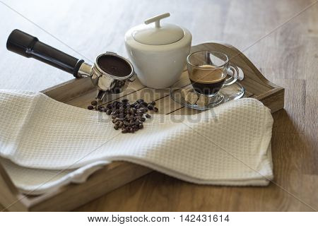Glass of espresso, brown sugar, coffee beans, grouphead and sugar bowl on a wooden tray