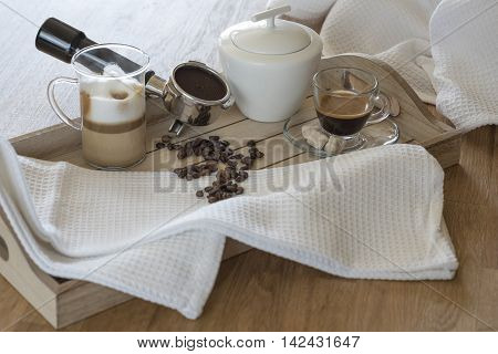 Wooden tray with glass of latte macchiato, espresso, grouphead, coffee beans and brown sugar