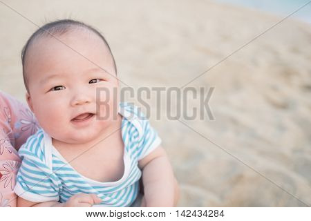 cute baby smile happily in adult arms in the beach asian