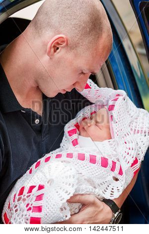 Young father holding his newborn daughter sitting on the back seat of the car