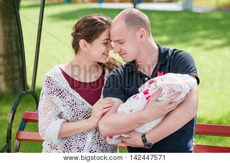 Happy Family Resting In A Park. Father Holding Newborn Daughter In Her Arms.