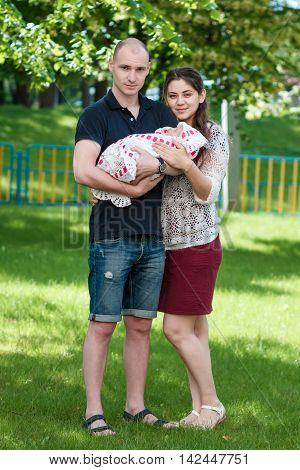Happy couple holding their newborn daughter in her arms. Outdoors