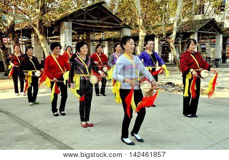Wan Jia China - October 29 2012: A women's waist drum band with red and yellow silk scarves rehearsing a routine in the town's market square