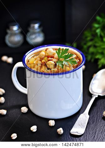 Soup with chickpeas, lentils, rice, beef in a bowl on a black background.