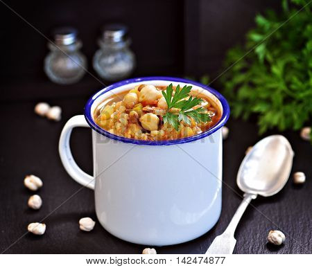Soup with chickpeas, lentils, rice, beef in a bowl on a black background.