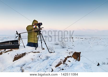 Man with photo camera on tripod taking timelapse photos in the arctic tundra. Poor lighting conditions.
