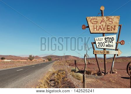 Deserted road  and tall vintage gas sign  in typical Moroccan landscape near Ouarzazate,  Morocco. Toned image.