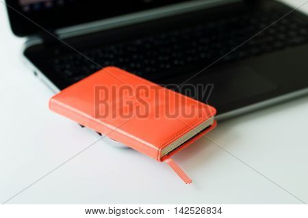 Red paper notebook on black computer. Small business diary and laptop on white office table. Business concept