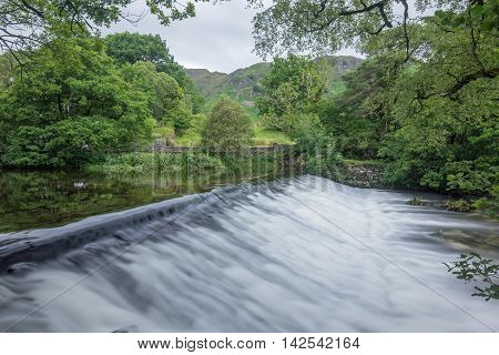 Great Langdale Beck weir at Elterwater near Ambleside in the Lake District National Park, Cumbria, England.  Photographed from the Cumbria Way footpath a popular walking route for tourists.