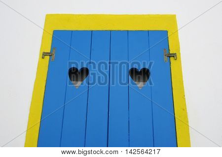 yellow window frame and blue wooden door with two hollow heart shape gaps of a house front in Moinhos village at Sao Miguel Azores island in Portugal in conceptual love and welcome concept