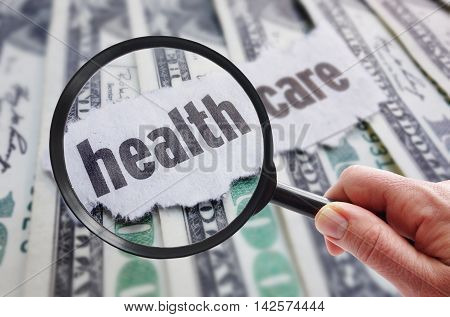 Magnifying glass looking at health care newspaper headline on cash