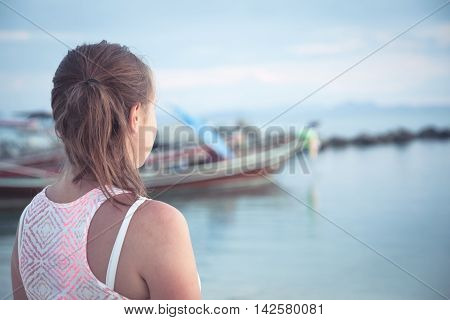 Teenager girl looking into the distance on tropical beach at sunset during summer holidays. Sunlight illuminate girl face