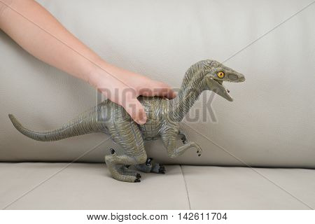 kids hand catching a greu Deinonychus toy on a sofa at home