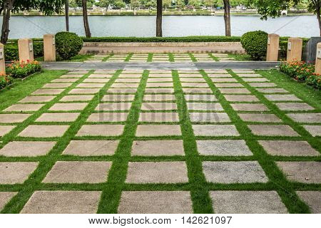 Pattern of square cement floor tiles with green grass blackground