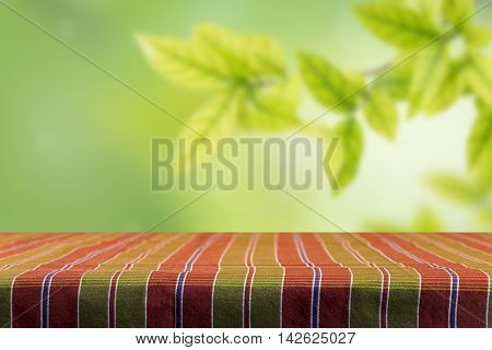 Empty table and tablecloth with blur green leaves bokeh background for product display montage