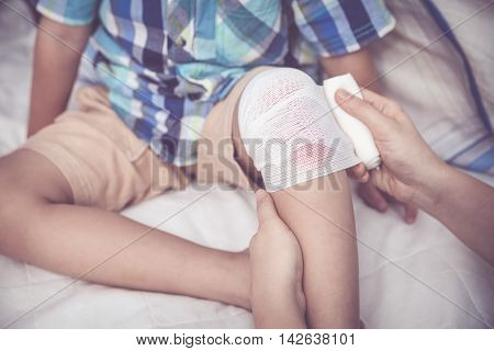 Child Injured. Mother Bandaging Son's Knee.  Vintage Tone Effect.