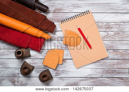 Brightly colored leather in rolls working tools shoe lasts notebook with pencil on white wooden background. Leather craft.