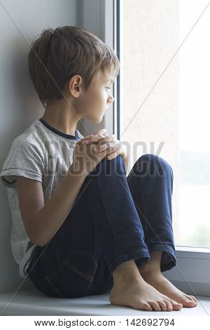 Sad lonely child by the window. Boy looking outdside.