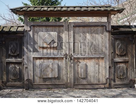 Old wooden gate with a wooden roof. Pavement from stone blocks