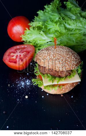 Hamburger with salad cheese tomato meat on black backdrop. Popular snack.