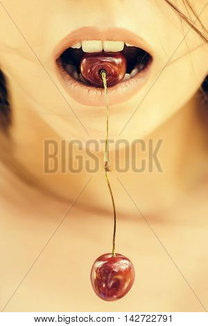 Red cherries pair hang from young woman mouth with rosy sensual lips