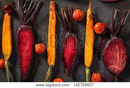 Baked carrots and beets with tomatoes on a baking tray top view