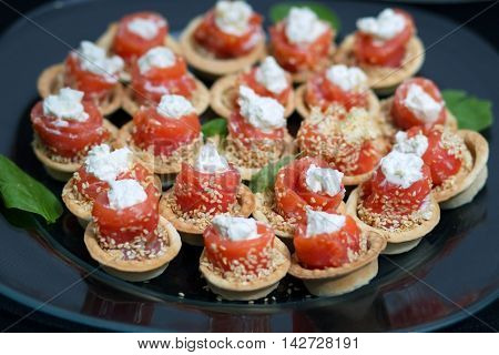 Salmon rolls stuffed with cheese sprinkled sesame seeds, laid on a transparent glass plate