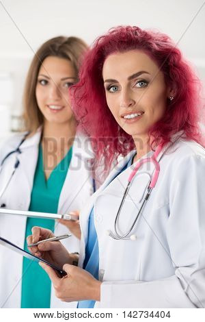 Portrait of two female doctors standing with clipboard and tablet ready to work. Health care medical service or education and teamwork concept.