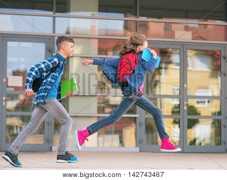 Happy children - boy and girl with books and backpacks on the first school day. Excited to be back to school after vacation. Full length outdoor portrait.