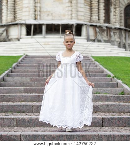 Portrait of a beautiful young little girl in white gown, summer outdoors