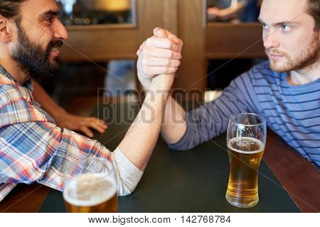 people, leisure, challenge, competition and rivalry concept - happy male friends arm wrestling and drinking draft beer at bar or pub