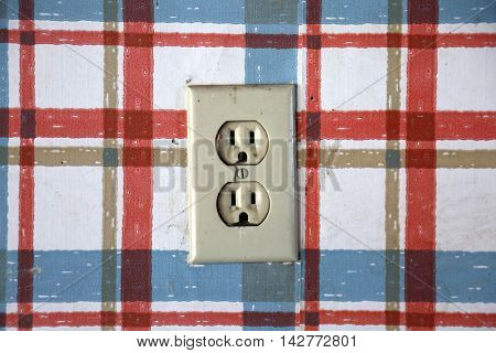 Old dangerous looking wall electrical socket on a plaid wall 