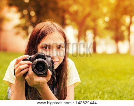 Young woman photographer with camera lie down on grass. Image with copyspace and sunkissed effect. Focus at camera. Shallow DOF
