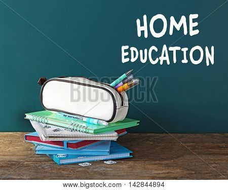 Home education concept. Pencil case with various stationery on table, on blackboard background