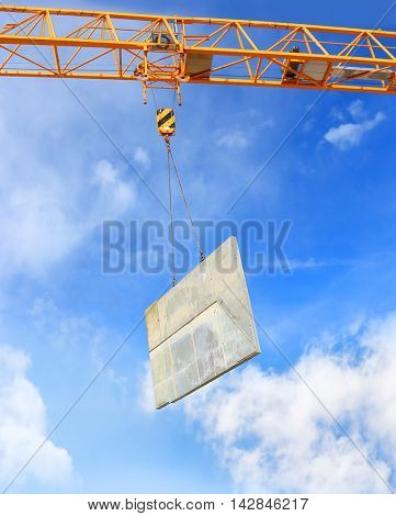 Yellow crane hook lifting load over clouds on blue sky. Construction industry background. 