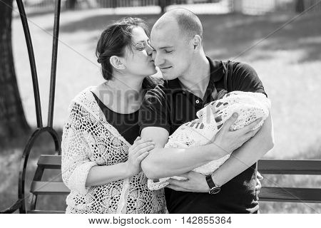 Young Mother Kissing Happy Father. Father Holding Newborn Daughter In His Arms. Outdoors.black And W