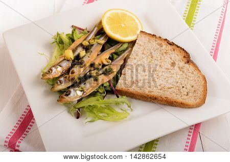 dried stint on salad with garlic and parsley a slice of bread and lemon on a plate