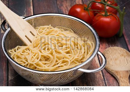 Spaghetti in a stainless steel collander on a wood surface