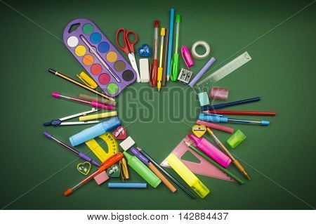 Different school supplies in heart shape on green background.