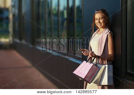 Smiling girl with shopping bags with phone in hand. Shopper. Sales.