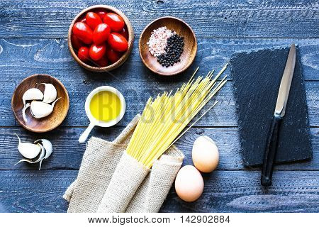 Top view of italian ingredients for tomato and basilic spaghetti with olive oil and garlic over a wood background.