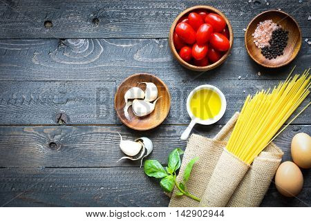 Top view of italian ingredients for tomato and basilic spaghetti with olive oil and garlic over a wood background.