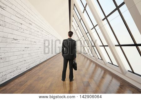 Businessman walking in clean corridor interior with dark wooden floor light wall concrete ceiling and panoramic window. 3D Rendering