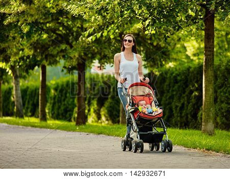 beautiful young woman pushing baby carriage in the park