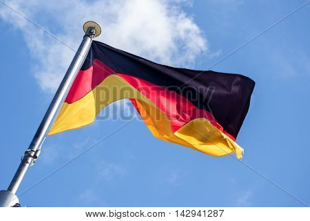 German flag fluttering in the wind against the blue sky with light clouds diagonal view from below soft motion blur
