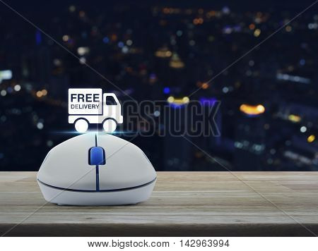 Wireless computer mouse with free delivery truck icon on wooden table over blur light city tower Transportation business concept